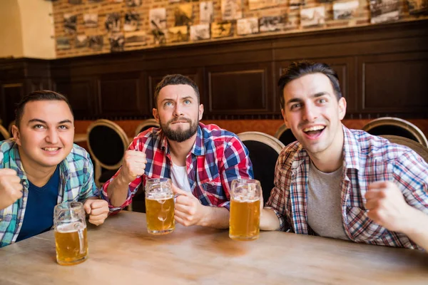 Grupo de jovens amigos bonitos assistindo TV e torcendo por sua equipe enquanto descansa no pub . — Fotografia de Stock