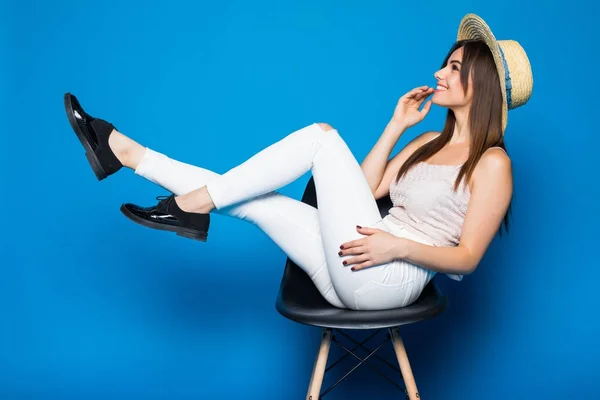 Jolie fille aux cheveux longs en chaise sur fond bleu en studio. Elle porte des vêtements d'été. Elle tient les jambes au-dessus et garde les yeux fermés . — Photo