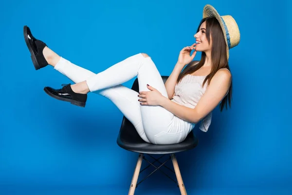 Jeune femme souriante assise sur une chaise sur fond bleu . — Photo