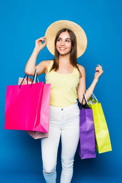 Divat portré fiatal mosolygó nő visel egy bevásárló táskák, szalmakalap alatt színes kék háttér — Stock Fotó