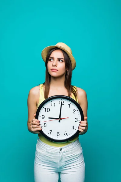 Giovane donna triste in possesso di un orologio che mostra quasi 9 con emozioni sconvolte su sfondo verde — Foto Stock