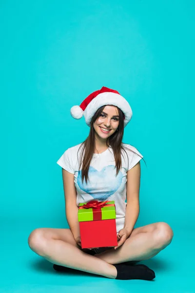 Портрет щасливої усміхненої дівчини в сукні, що тримає подарункову коробку, сидить на підлозі ізольовано на зеленому фоні — стокове фото
