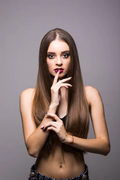 Glimlachend meisje met natuurlijke make-up, de vinger op de lippen, de schone huid en witte tanden op grijze achtergrond — Stockfoto