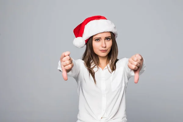 Schattig triest Kaukasische tienermeisje dragen Kerstman hoed en handschoenen tonen duimen naar beneden en trieste gezichtsuitdrukking geïsoleerd op grijze achtergrond maken. — Stockfoto