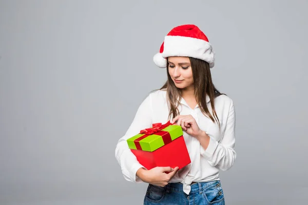 Noel hediye gülümseyen mutlu ve heyecanlı tutan gri arka plan üzerinde Santa şapka Noel kadın — Stok fotoğraf