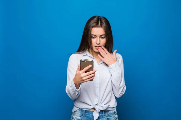 Woman feeling shock reading on mobile phone on blue background — Stock Photo, Image