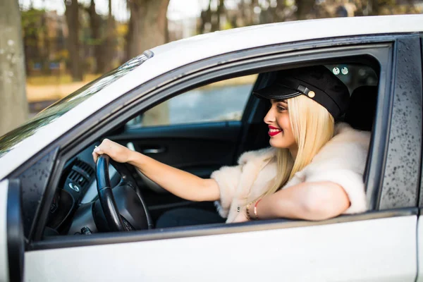 Conduciendo por la ciudad. Mujer joven sonriendo y mirando recto mientras conduce un coche — Foto de Stock