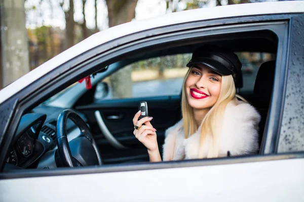 Primer plano retrato feliz, sonriente, atractiva mujer, comprador sentado en su nuevo coche blanco que muestra las llaves aisladas al aire libre concesionario calle mucho fondo . — Foto de Stock