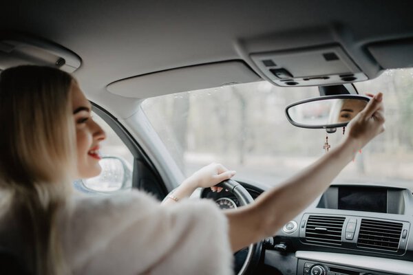 Pretty young woman looking in mirror while driving car in the road