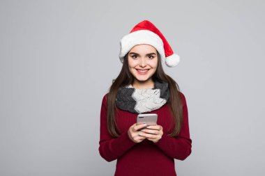 Cep telefonuyla gri arka plan üzerinde izole kırmızı Noel Baba genç esmer bir kadın portresi