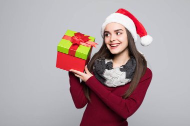 Heyecanlı sürpriz kadın kırmızı Noel Baba kıyafeti holding içinde yığın gri arka plan üzerinde izole hediye