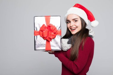 Heyecanlı sürpriz kadın kırmızı Noel Baba kıyafeti holding içinde yığın gri arka plan üzerinde izole hediye
