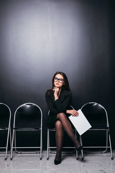 Attraente bella vestito studentessa tenuta file riunione seduta sulla sedia e guardando zona vuota pensare pianificazione del lavoro sentirsi frustrati in camera parete nera . — Foto Stock