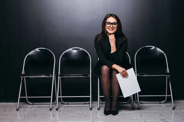 Ελκυστικές όμορφο κοστούμι αρχείο φοιτήτριας εκμετάλλευση meeting κάθεται σε καρέκλα και να ψάχνει στην κενή περιοχή σκέψης εργασία σχεδιασμού αισθάνονται απογοητευμένοι στο μαύρο τοίχο δωμάτιο. — Φωτογραφία Αρχείου