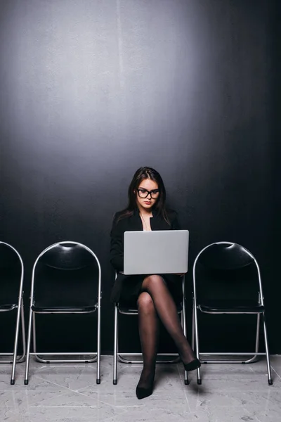 Зосереджена бізнес-леді, що працює на ноутбуці, чекаючи інтерв'ю, сидячи на стільці — стокове фото