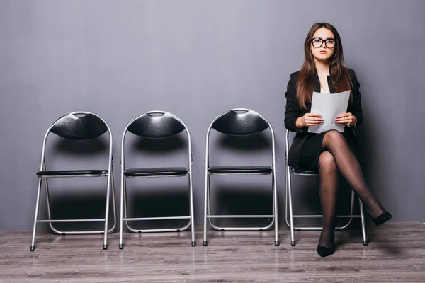 Waiting for interview. Confident young businesswoman holding paper while sitting on chair against grey background