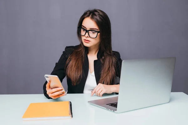 オフィスのコンピュータの近くでスマートフォンを使用して若い笑顔のビジネス女性 — ストック写真