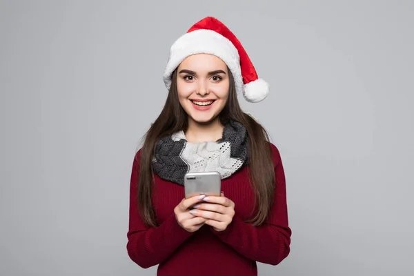 Cep telefonuyla gri arka plan üzerinde izole kırmızı Noel Baba genç esmer bir kadın portresi — Stok fotoğraf