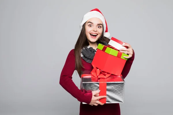 Heyecanlı sürpriz kadın kırmızı Noel Baba kıyafeti holding içinde yığın gri arka plan üzerinde izole hediye — Stok fotoğraf