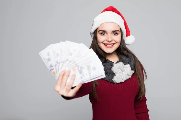 Noel Baba şapkası gri arka plan üzerinde izole para ile mutlu genç gülümseyen kadın. — Stok fotoğraf