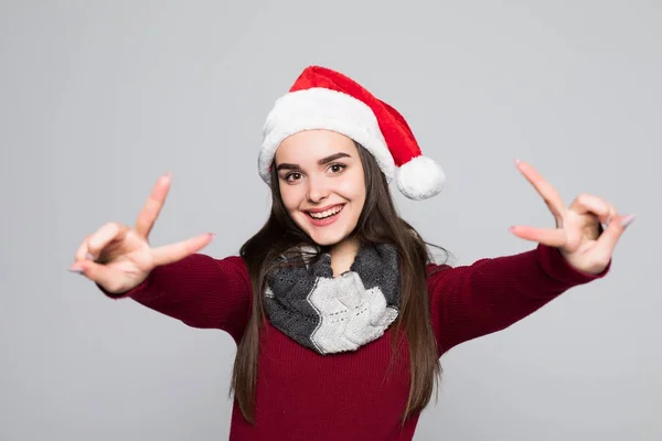 Portret van een vrolijk lachende meisje in KERSTMUTS tonen vrede gebaar en kijken naar camera geïsoleerd over grijze achtergrond — Stockfoto