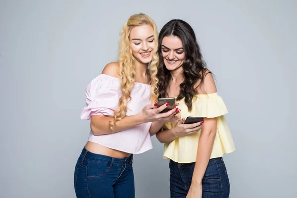 Internetsüchtig. zwei junge beste Freundinnen beschäftigen sich in sozialen Netzwerken mit ihren Mobiltelefonen, tragen lässige Hemden, isoliert auf weißem Hintergrund — Stockfoto