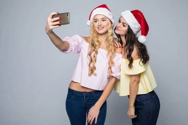 Dos mujeres toman selfie de las manos en sombrero de santa aislado sobre fondo blanco. Humor de Navidad —  Fotos de Stock
