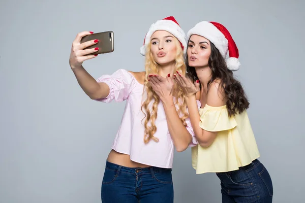 2 つの女性は、白い背景で隔離のサンタ帽子の手から selfie を取る。クリスマス気分 — ストック写真