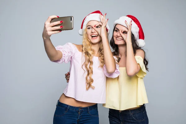 Dos mujeres toman selfie de las manos en sombrero de santa aislado sobre fondo blanco. Humor de Navidad —  Fotos de Stock