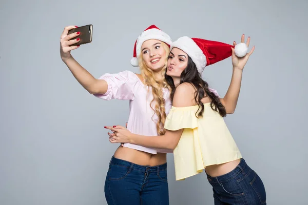 Due donne scattano selfie da mani in cappello di Babbo Natale isolato su sfondo bianco. L'umore di Natale — Foto Stock
