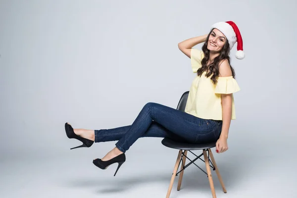 Mutlu kadın beyaz bir arka plan üzerinde izole sandalyede oturup Noel Baba hatwith hediye kutusu — Stok fotoğraf