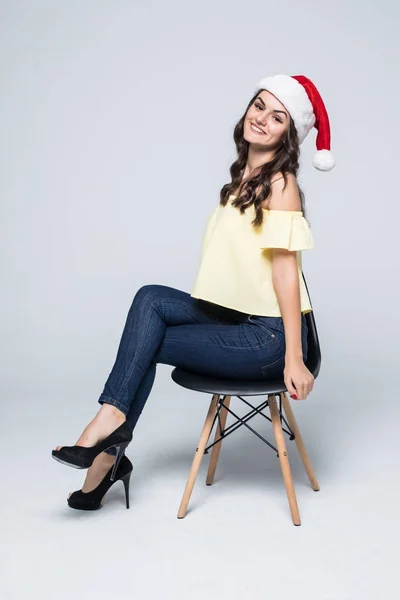 Femme heureuse dans le chapeau du Père Noël avec boîte cadeau assis dans la chaise isolé sur un fond blanc — Photo