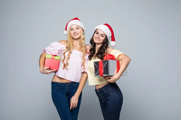 Two happy women in santa hats with gift boxes standing on white background — Stock Photo, Image