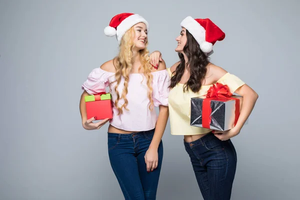 Дві щасливі жінки в капелюхах Санти з подарунковими коробками, що стоять на білому тлі — стокове фото