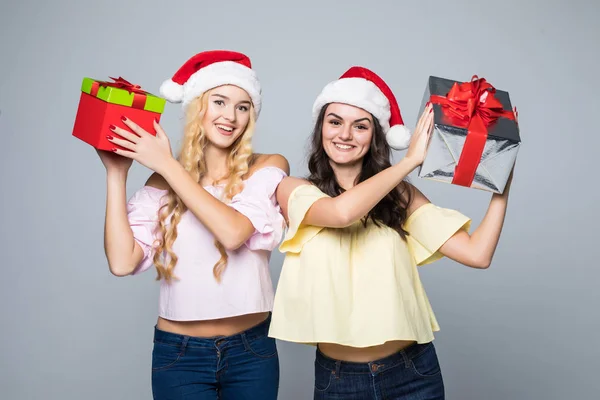 Дві щасливі жінки в капелюхах Санти з подарунковими коробками, що стоять на білому тлі — стокове фото