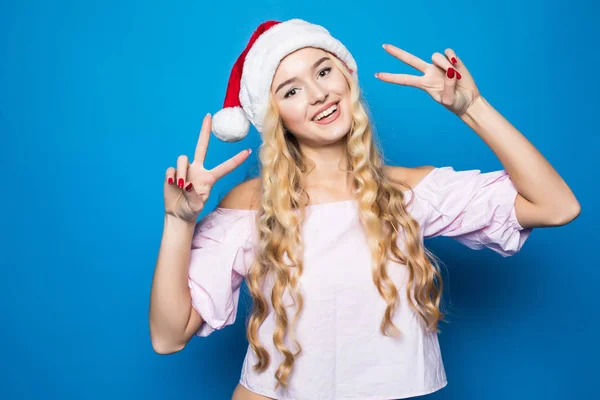 Alegre joven sonriente dama en sombrero de santa mostrando señal de victoria. Ella está aislada sobre fondo azul vivo, plano de estudio —  Fotos de Stock