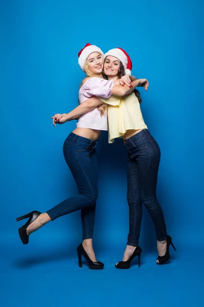 Portret van vrolijke gelukkig vrouwen in Kerstmis hoeden terwijl permanent en kijken naar camera geïsoleerd op blauwe achtergrond — Stockfoto