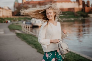 Güzel sarışın genç kadın günbatımında nehir kenarında yürüyüş gülümseme ve kamera üzerinde oynamak eğlenceli var