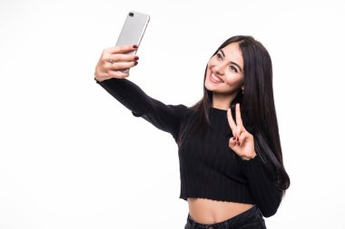Güzel genç kadın selfie fotoğraf zafer hareketi ile smartphone ile beyaz arka plan üzerinde yapıyor