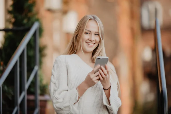 Великолепная красивая молодая женщина с блондинистыми волосами на смартфоне на фоне городской улицы . — стоковое фото