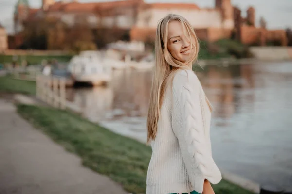 Hermosa mujer joven rubia caminando junto al río al atardecer divertirse sonrisa y jugar en la cámara —  Fotos de Stock