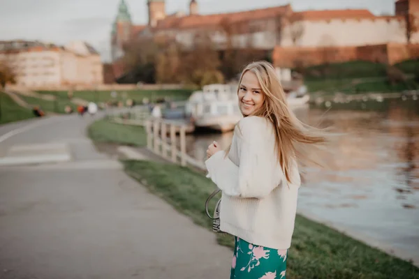 Güzel sarışın genç kadın günbatımında nehir kenarında yürüyüş gülümseme ve kamera üzerinde oynamak eğlenceli var — Stok fotoğraf