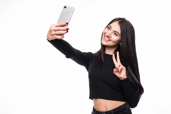 Belle jeune femme fait selfie photo avec geste de victoire avec smartphone sur fond blanc — Photo