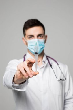 Beyaz bir arka plan üzerinde beyaz bir ceket bir şırınga tutarak onun yüzünde maske ile genç bir doktor izole
