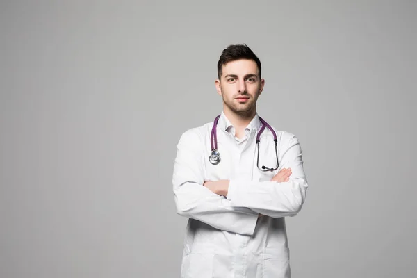 Retrato de médico sonriente de pie con las manos cruzadas aisladas sobre fondo gris —  Fotos de Stock