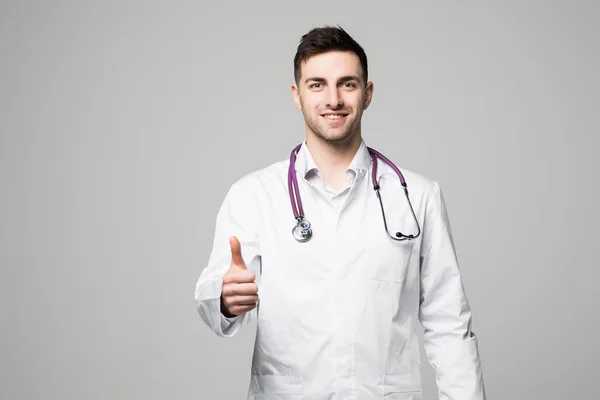 Retrato de cerca de un alegre doctor sonriente con estetoscopio mostrando los pulgares hacia arriba aislados sobre fondo blanco —  Fotos de Stock