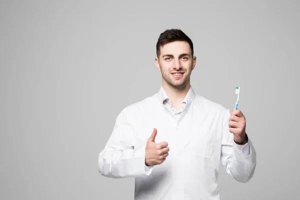 Dentysta uśmiechający się trzymając szczoteczkę do zębów i pokazano kciuki gest na białym tle — Zdjęcie stockowe