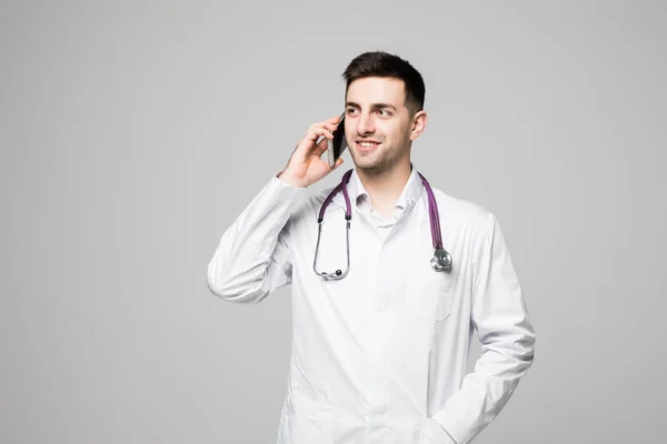 Портрет красивого молодого врача, разговаривающего по телефону на белом фоне — стоковое фото