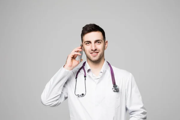Portrét pohledný mladý lékař mluvil telefonicky izolovaných na bílém pozadí — Stock fotografie