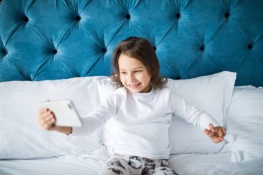 Yatakta yatan küçük kız alma selfie smartphone cep telefonu ile gülümseyen güzel
